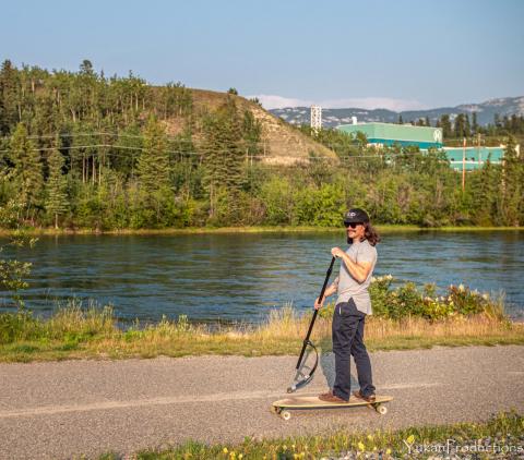 Joel Brennan rides a longboard along the waterfront trail using the SUPStick he invented
